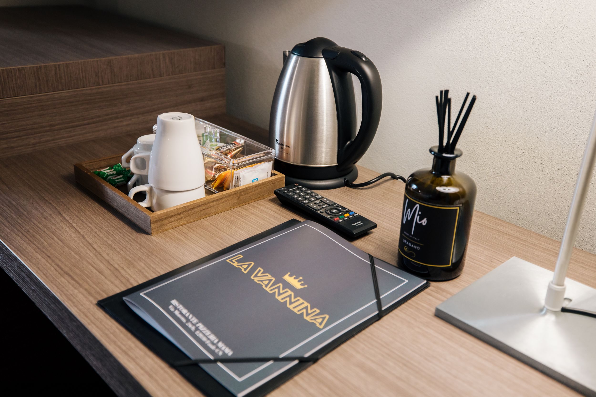 A modern workspace setup featuring a dark desk mat, white coffee mug, and reed diffuser against a wooden desktop surface.