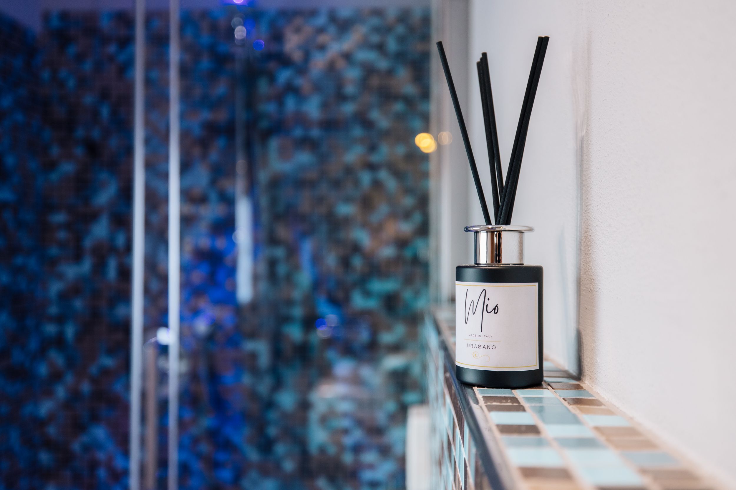 Black reed diffuser with dark liquid sits elegantly on white surface against blurred blue background.