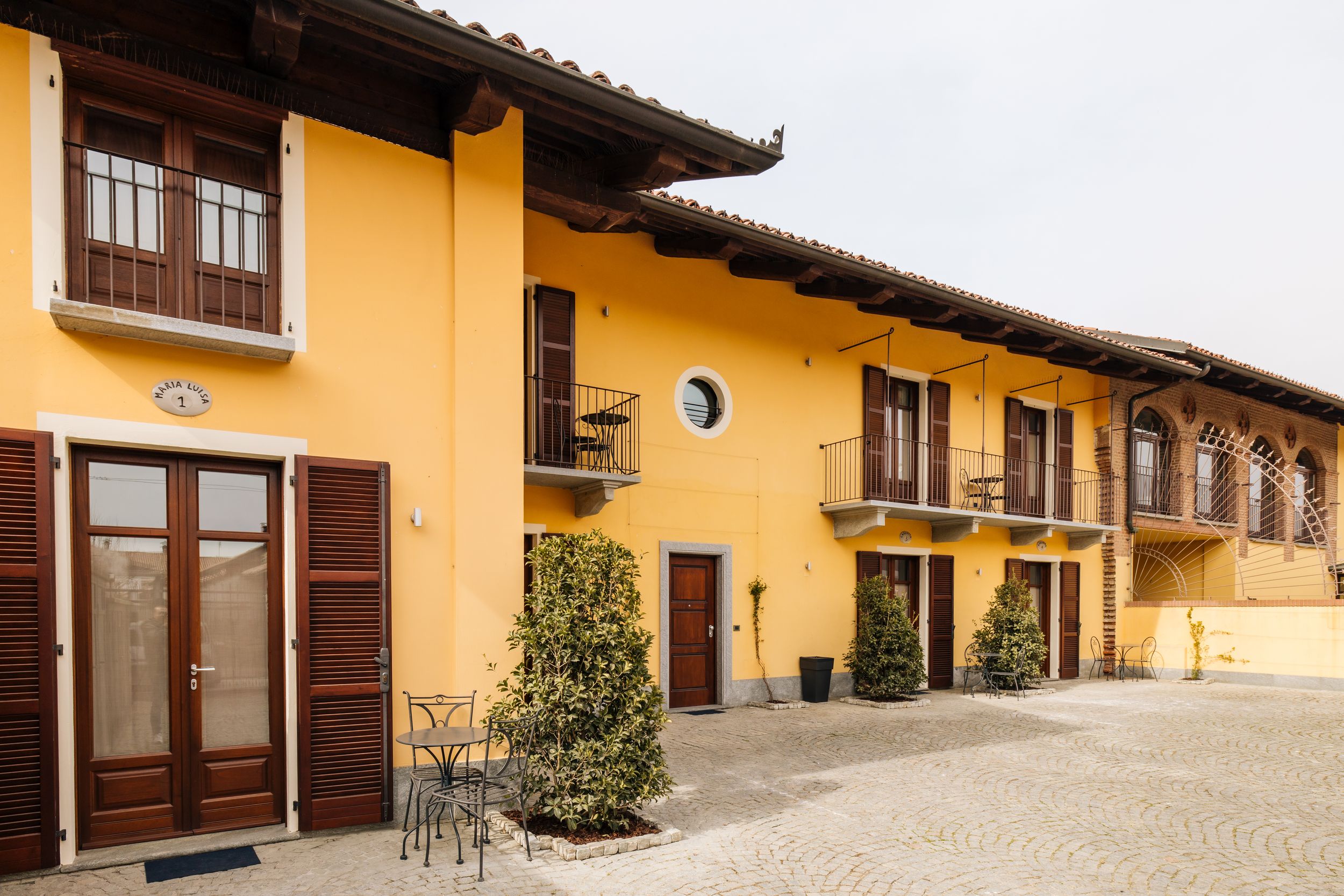 Modern yellow apartment complex exterior with brown shutters and cobblestone courtyard in Mediterranean style.