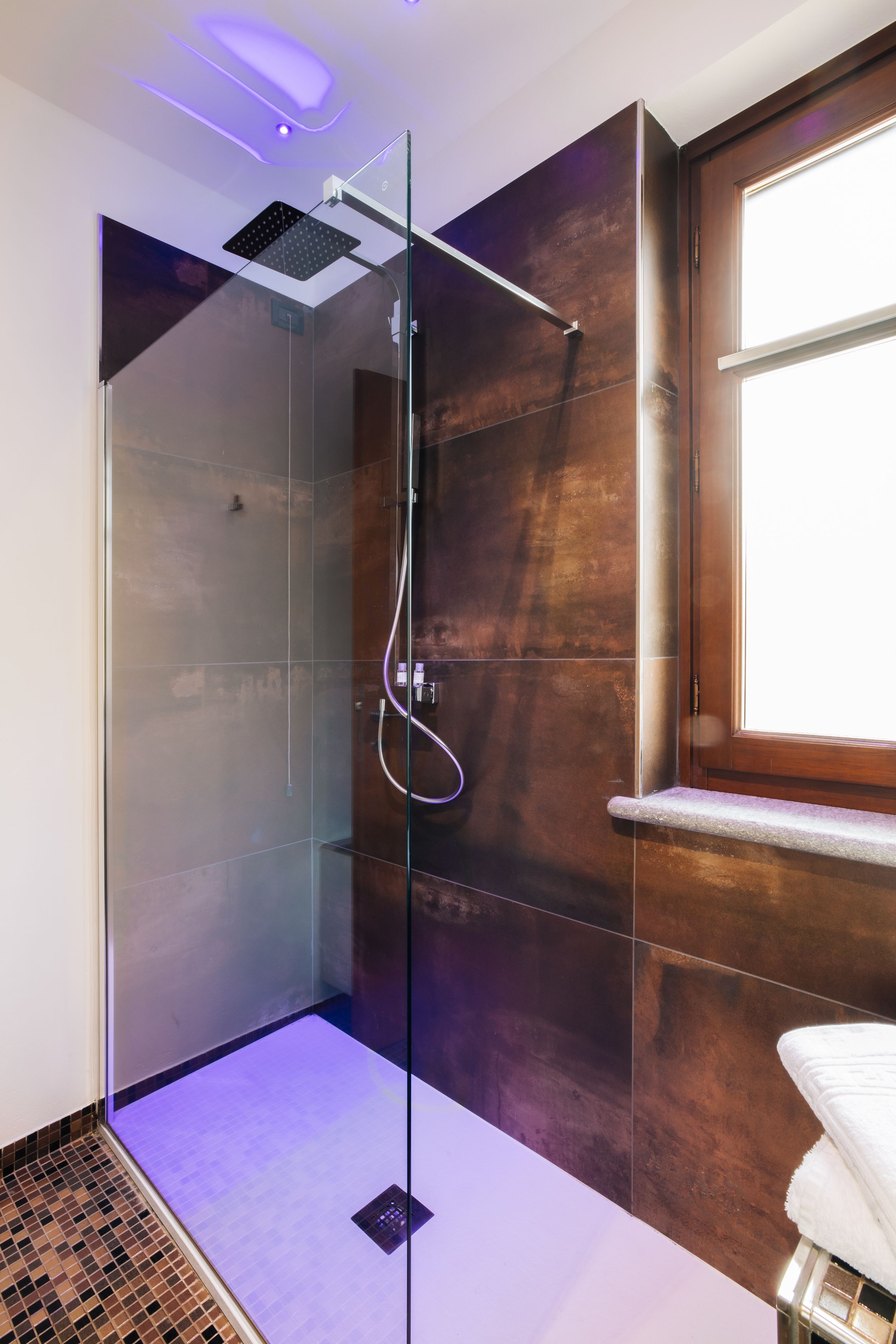 Modern walk-in shower with glass panel, LED lighting, and rustic brown tile walls in contemporary bathroom design.