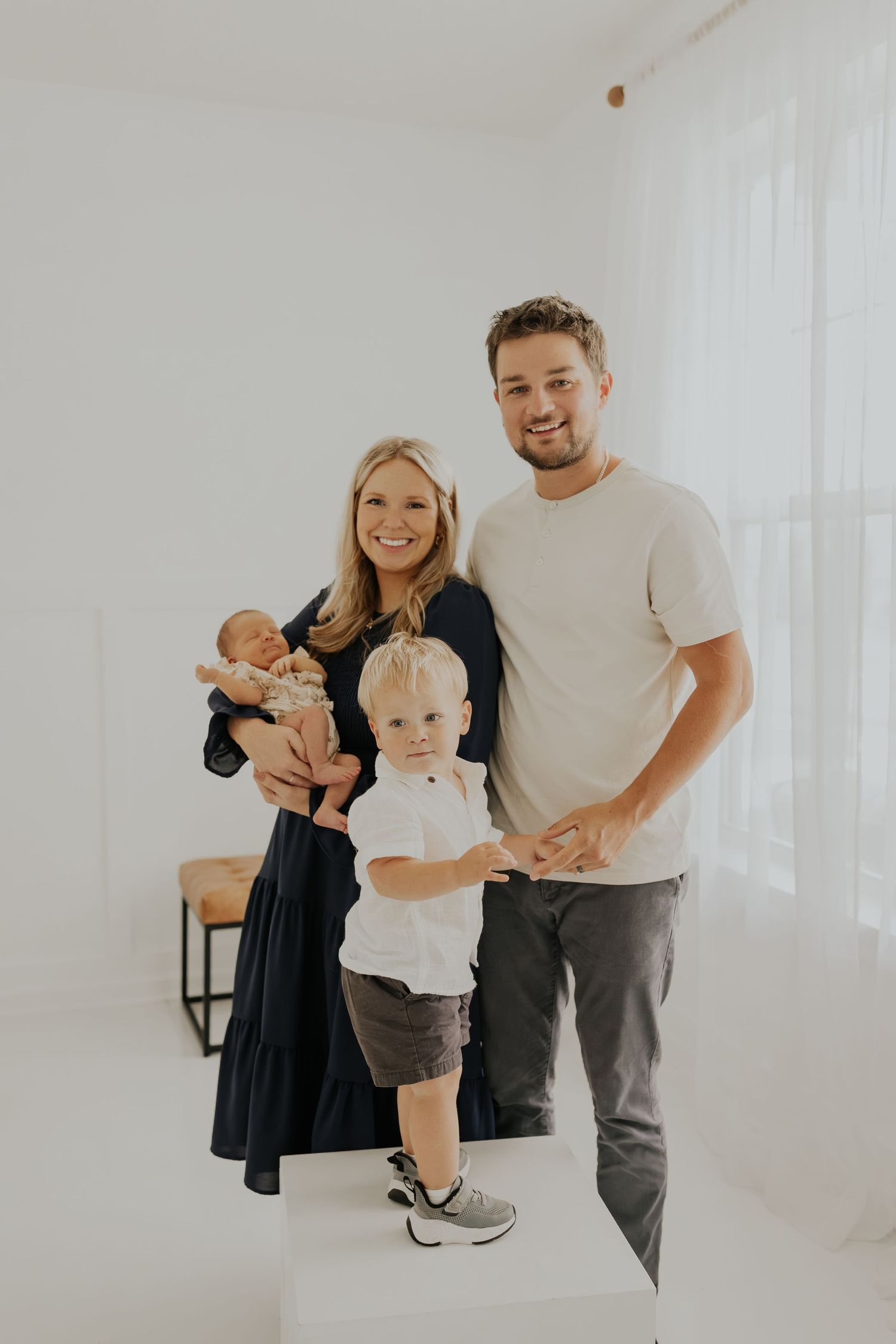 A family poses together in a bright white room wearing casual clothes for a minimalist portrait session.