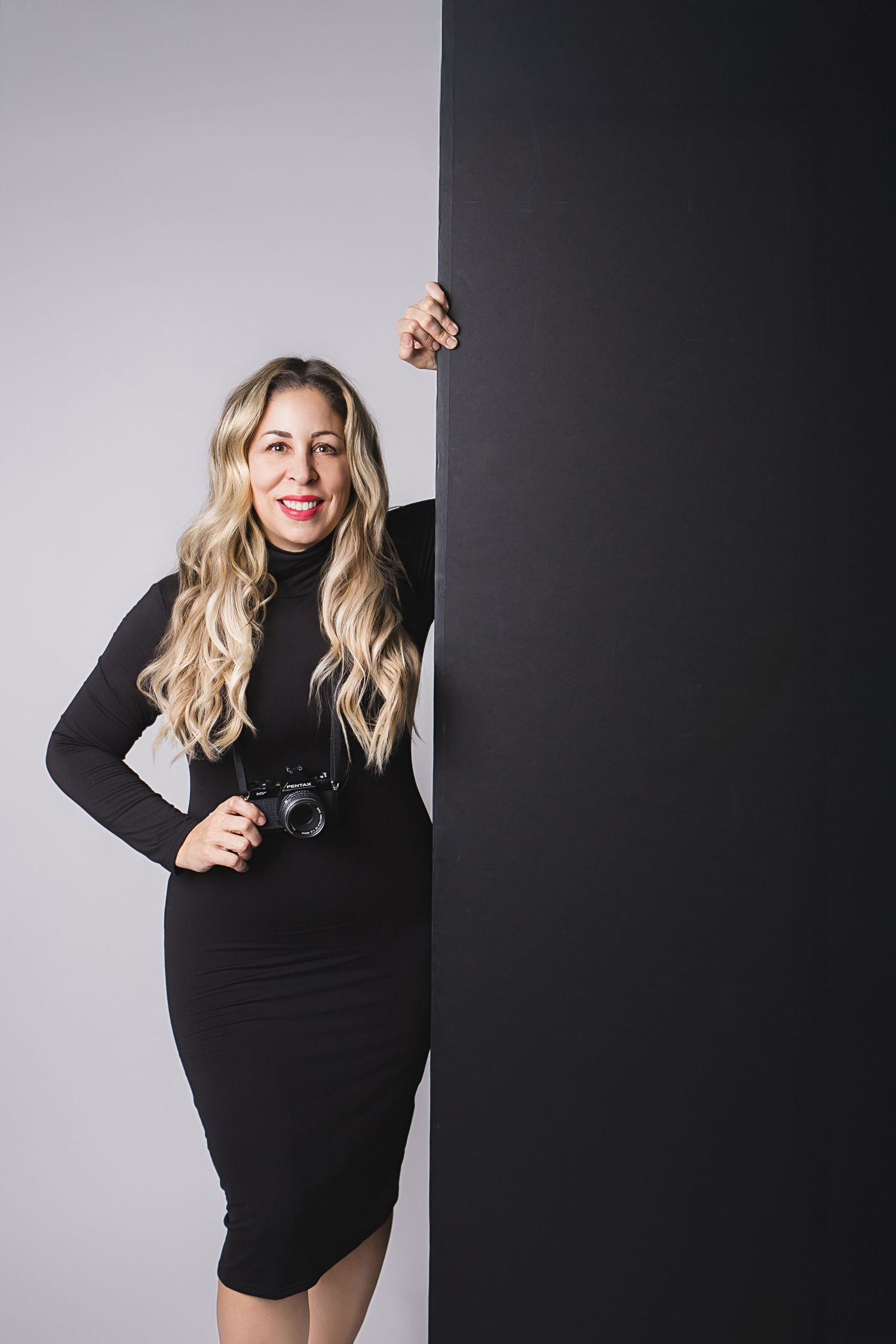 Studio fashion portrait of someone posing in a black sweater dress against a light gray background.