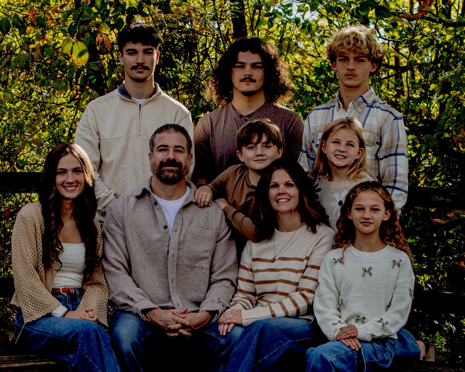 A family sits together outdoors on wooden steps surrounded by autumn foliage for a casual portrait session.
