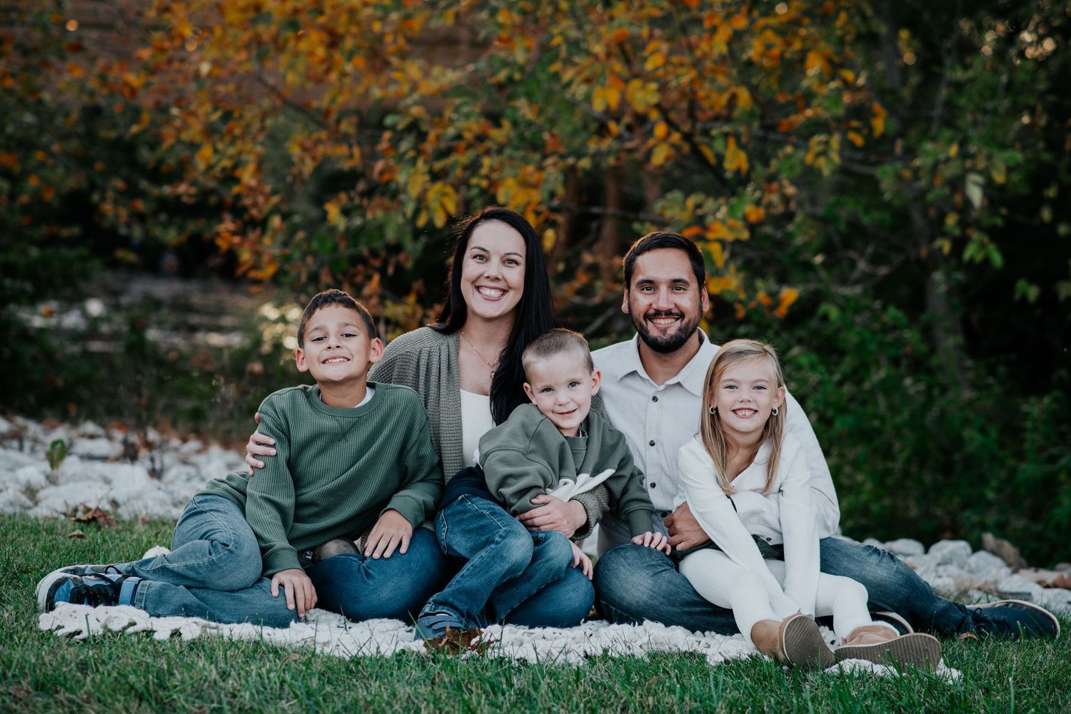 A family relaxes together on a blanket outdoors during an autumn photoshoot session.