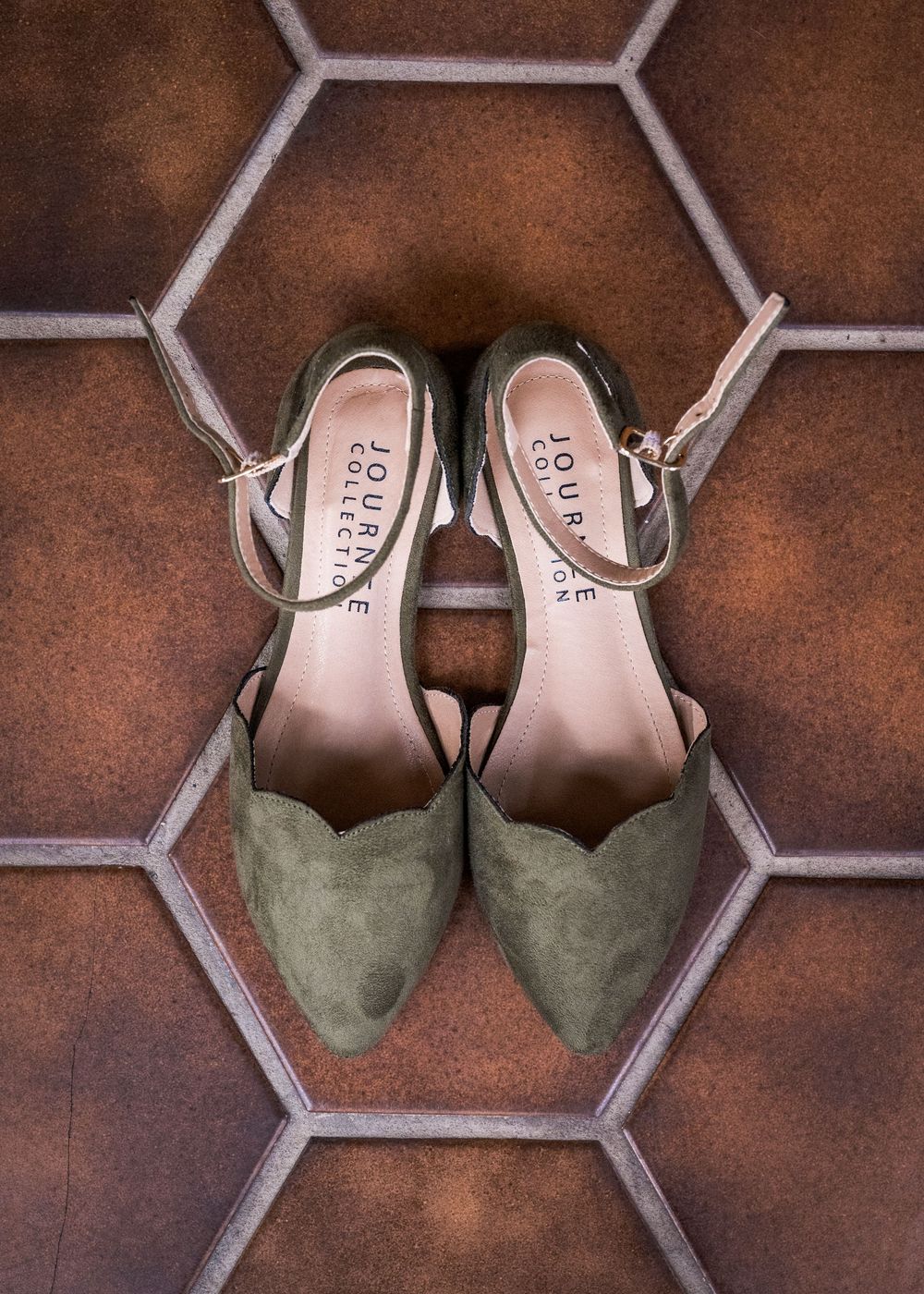Olive green suede Journey Collection pointed-toe heels with ankle strap on hexagonal tile floor.
