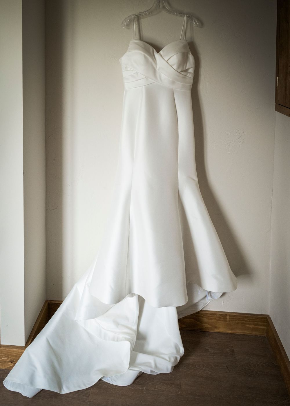 Elegant white satin mermaid wedding dress with sweetheart neckline and train hanging on display.