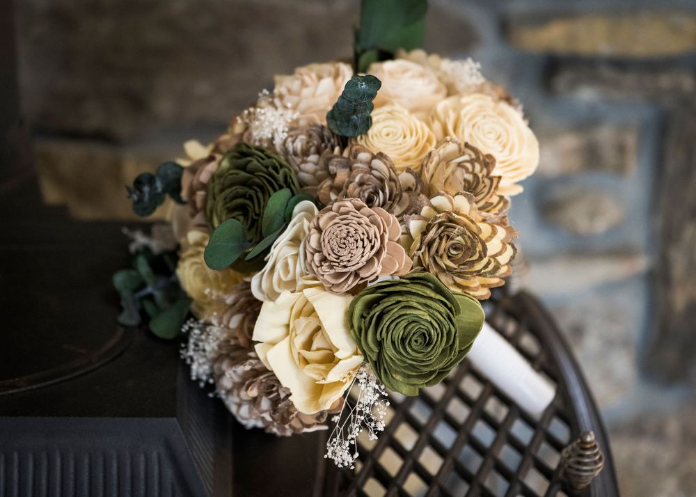An elegant bridal bouquet featuring cream, green, and taupe sola wood flowers with eucalyptus on a dark chair.