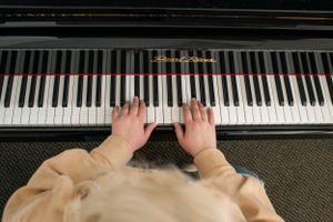 Hands playing piano keys on black upright piano in cream colored sweater.