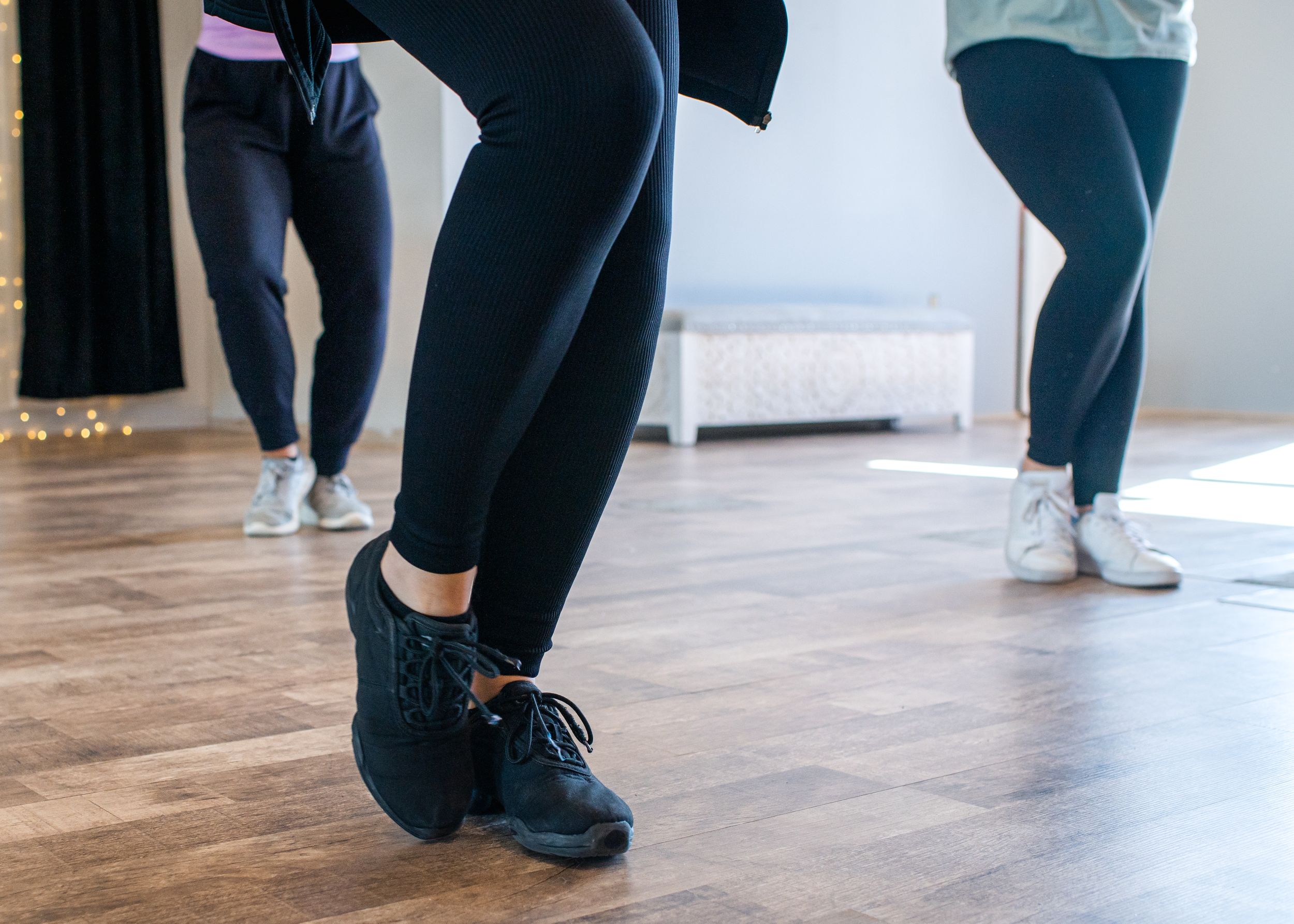 Close-up of feet in black athletic shoes and leggings on a wooden dance floor during exercise.