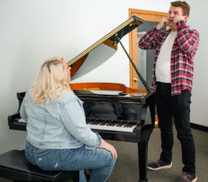 Voice lesson taking place at a grand piano in a bright music studio.