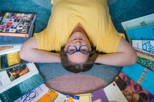 Overhead view of someone lying on floor surrounded by scattered books and photographs.