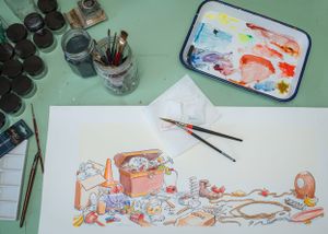 Artistic workspace with watercolor palette, brushes and whimsical illustration.