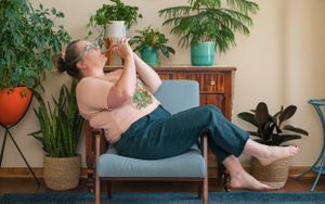 Person relaxing on chair among houseplants while enjoying a refreshing drink.