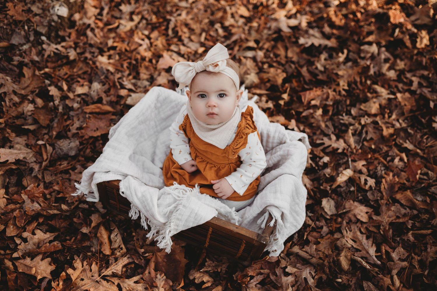 A person in white clothing lies among scattered autumn leaves on the ground during a fall photo session.