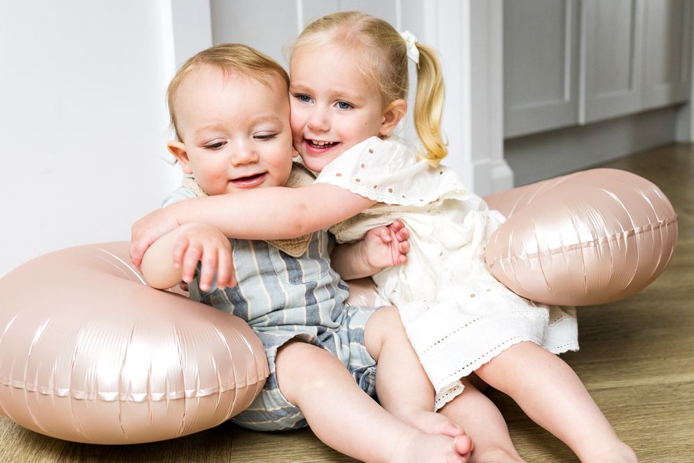 baby brother and big sister sitting together on the floor hugging