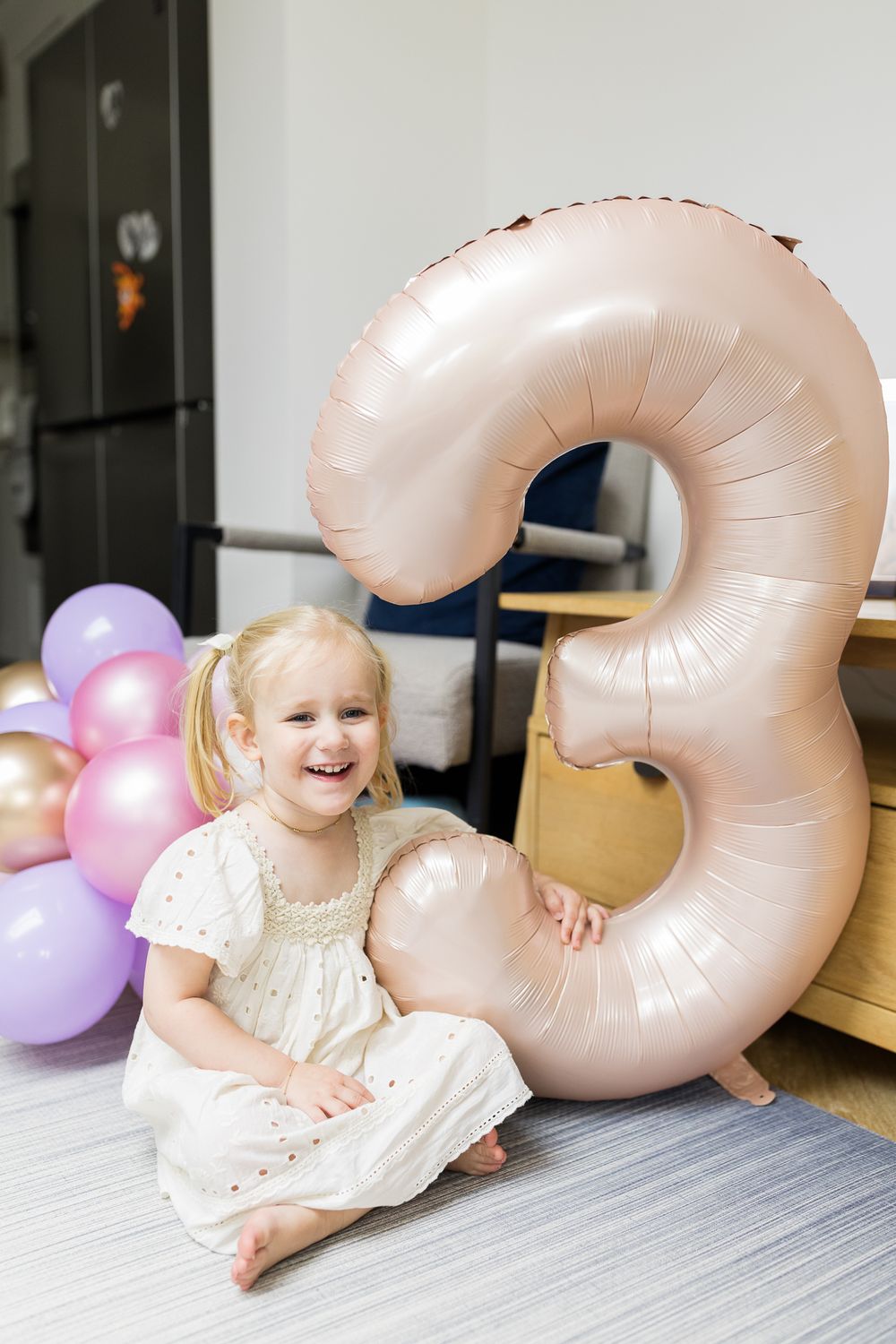 birthday girl sitting on the floor with big helium balloon with number three