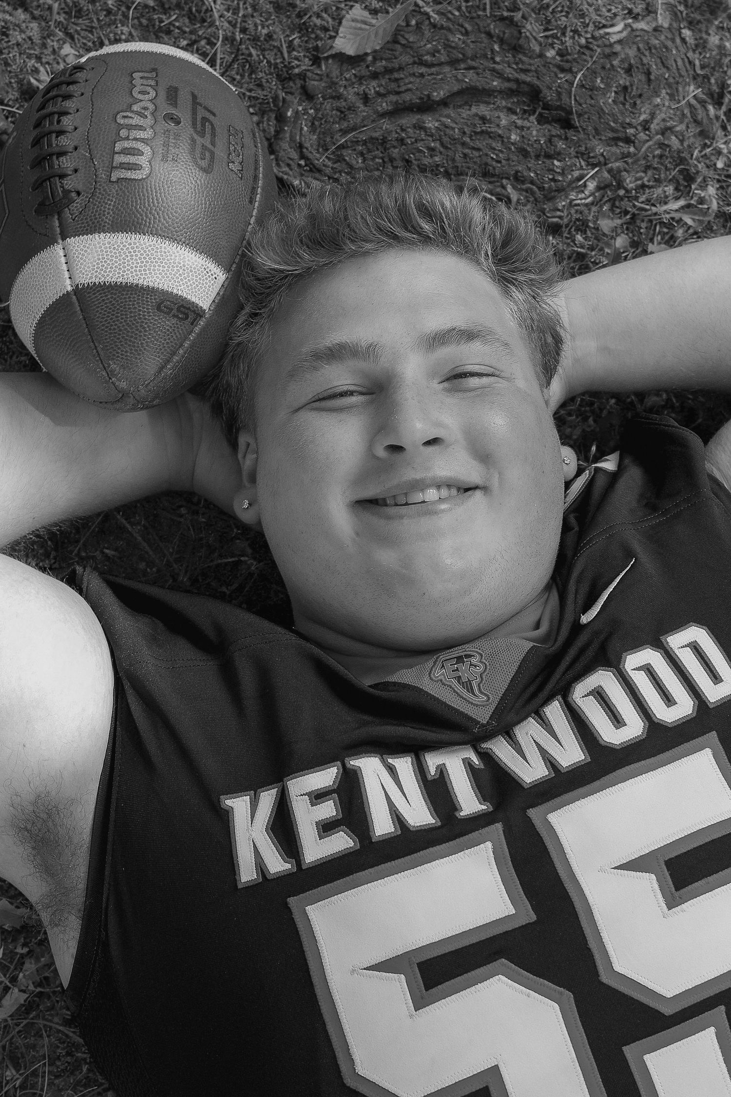 Black and white photo of a football player lying on grass with a Wilson football, wearing a Kentwood jersey number 55.