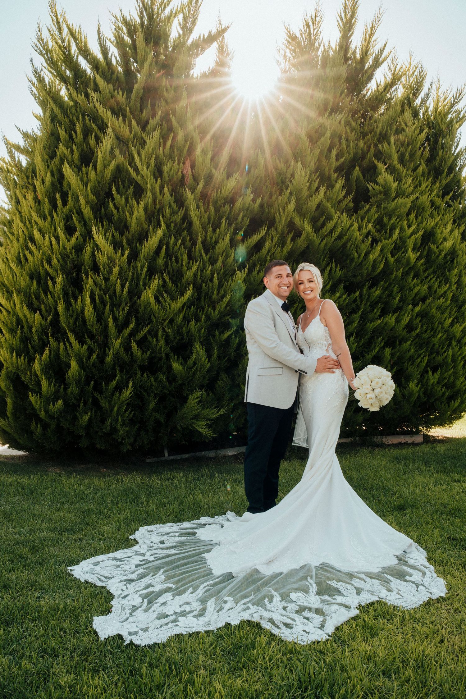 A romantic wedding moment captured among lush greenery with two people embracing in formal attire.