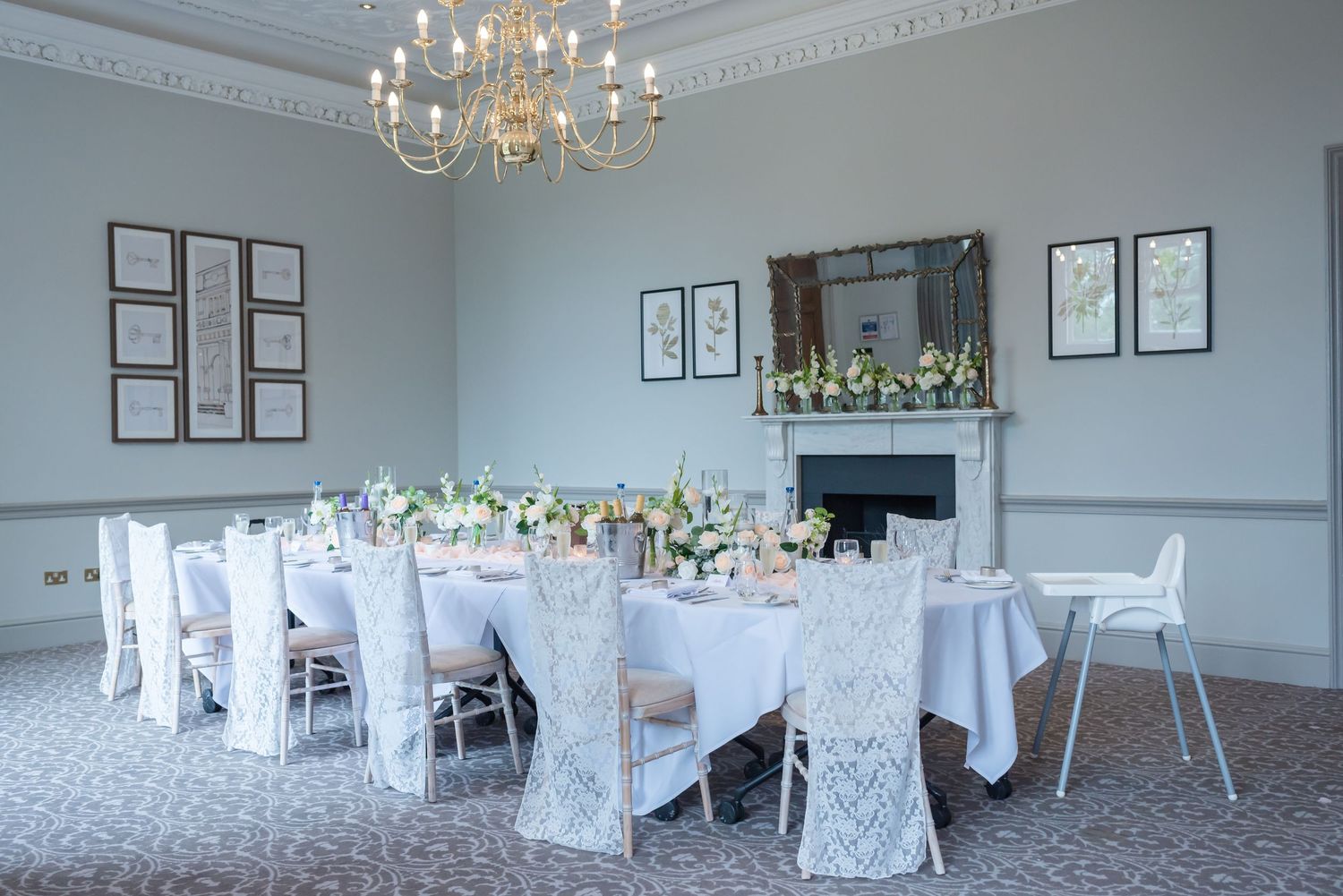 Elegant wedding reception venue with white tablecloths, chandeliers, and floral centerpieces in a bright room.