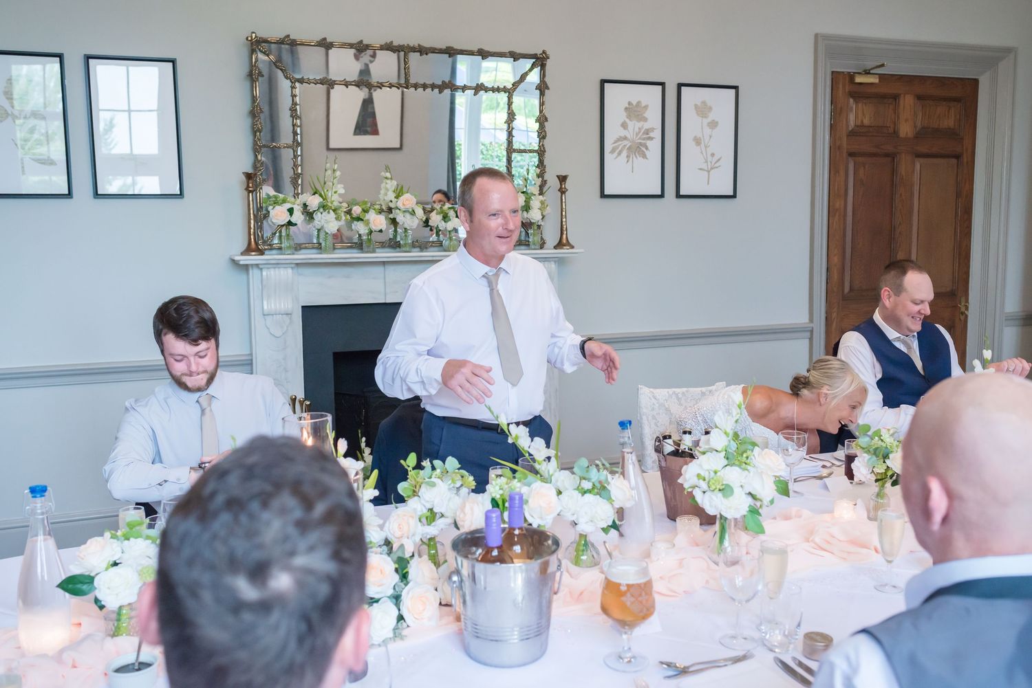 Wedding reception dining room with round tables set for guests and framed artwork on light blue walls.