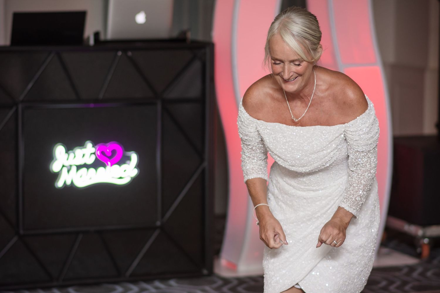 A series of wedding reception photos showing a white wedding dress and decor against a pink-lit backdrop.