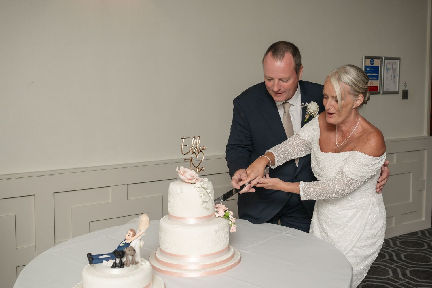 A couple in formal attire cuts their elegant three-tiered white wedding cake together at their reception.