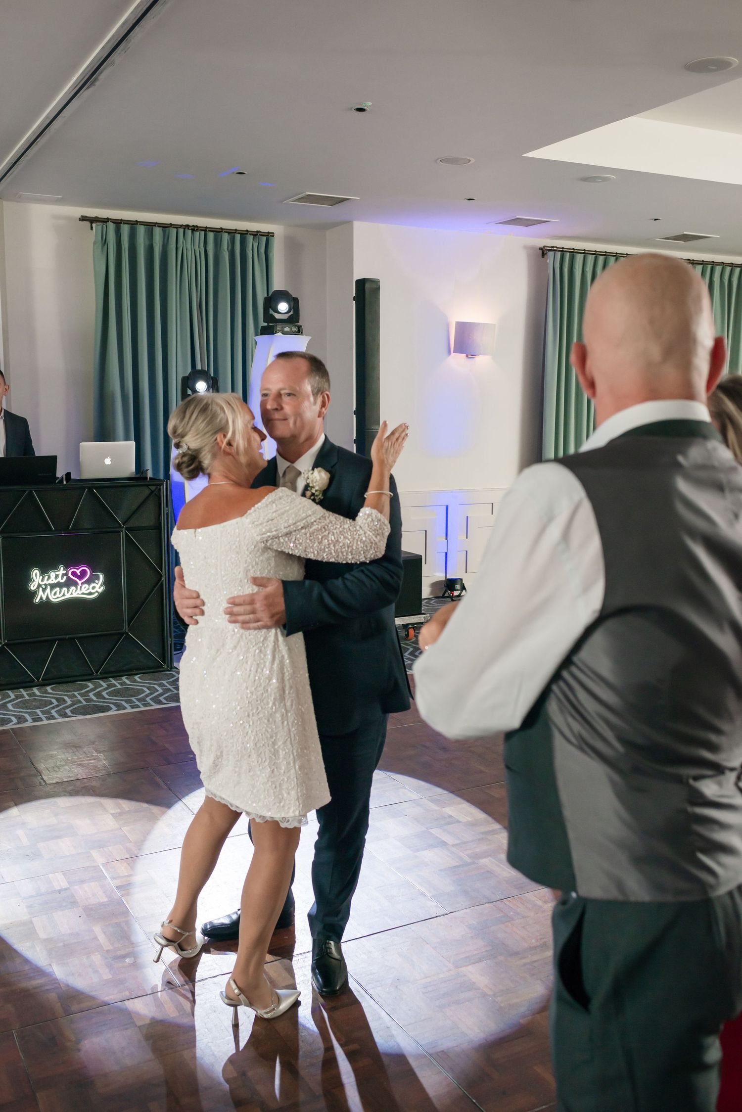 A couple performs a romantic dance move sequence on a white dance floor with teal curtains in the background.