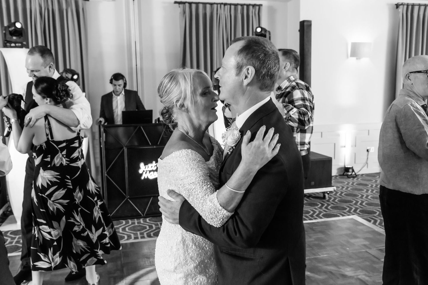 Wedding reception guests dancing in pairs on a hardwood floor under soft lighting.