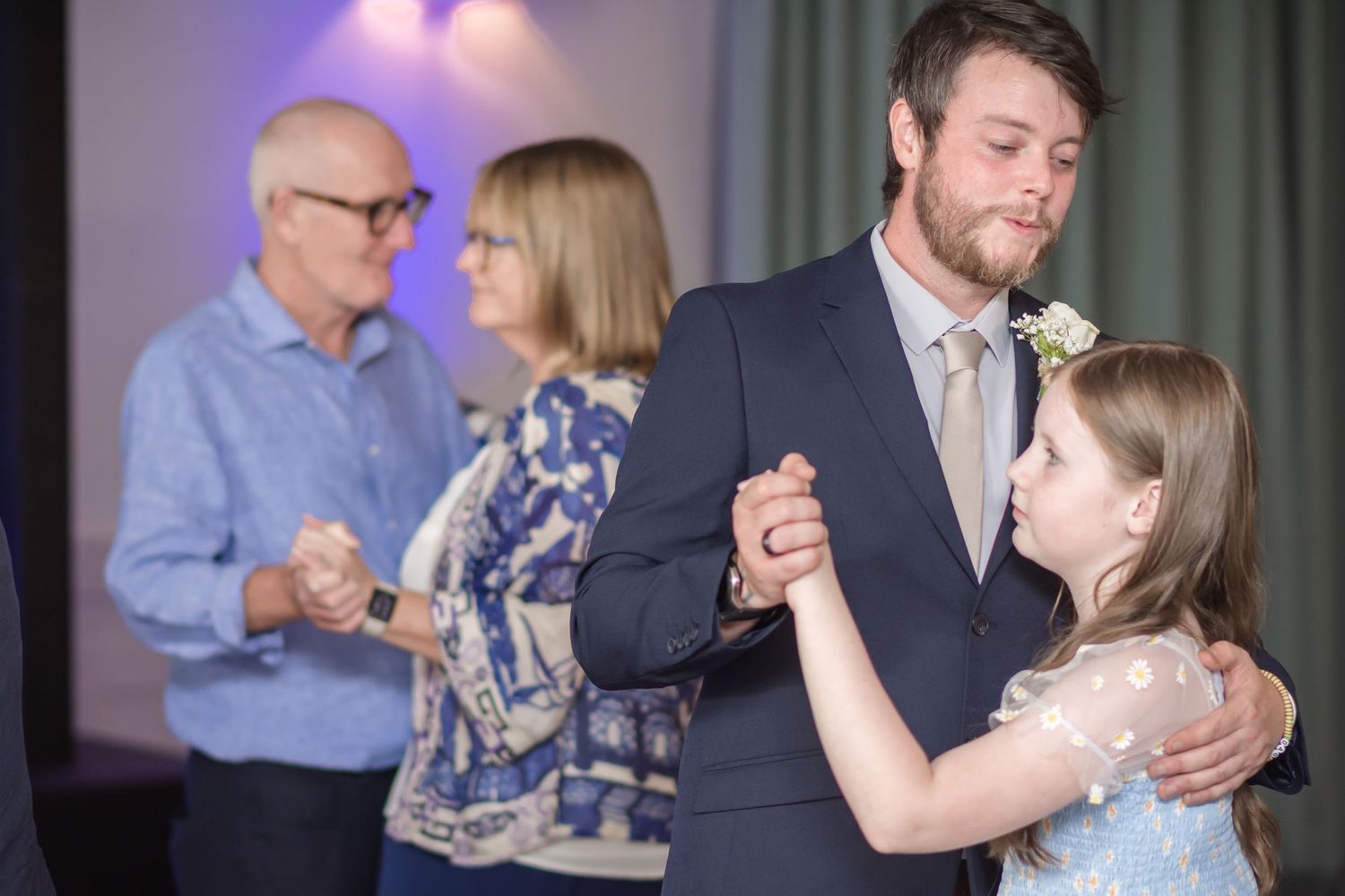 A couple dances together at a formal event under purple lighting.
