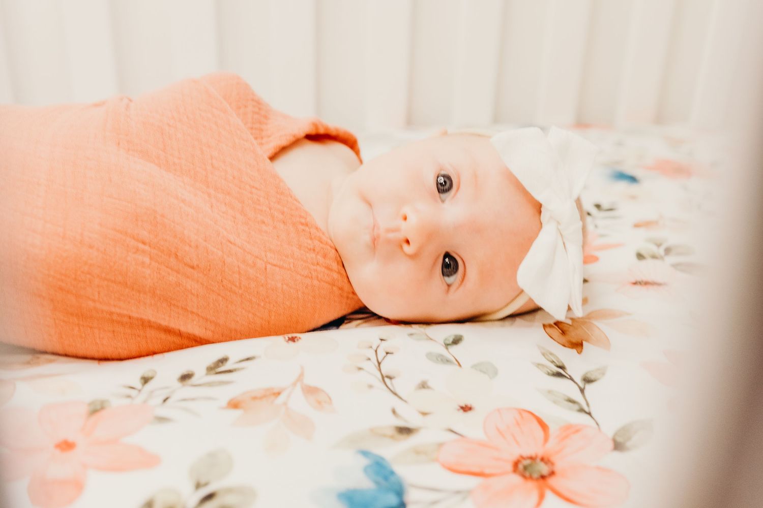 Baby lying on floral bedding with soft peach-colored lighting.