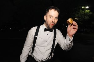 A person in a white dress shirt holds up a credit card while standing in a dark outdoor setting.