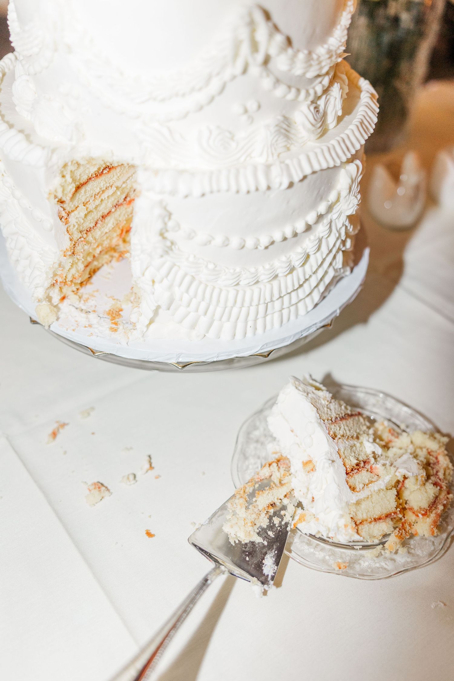 White wedding cake with delicate piped details and crumbs scattered on white surface showing slices being cut and served.