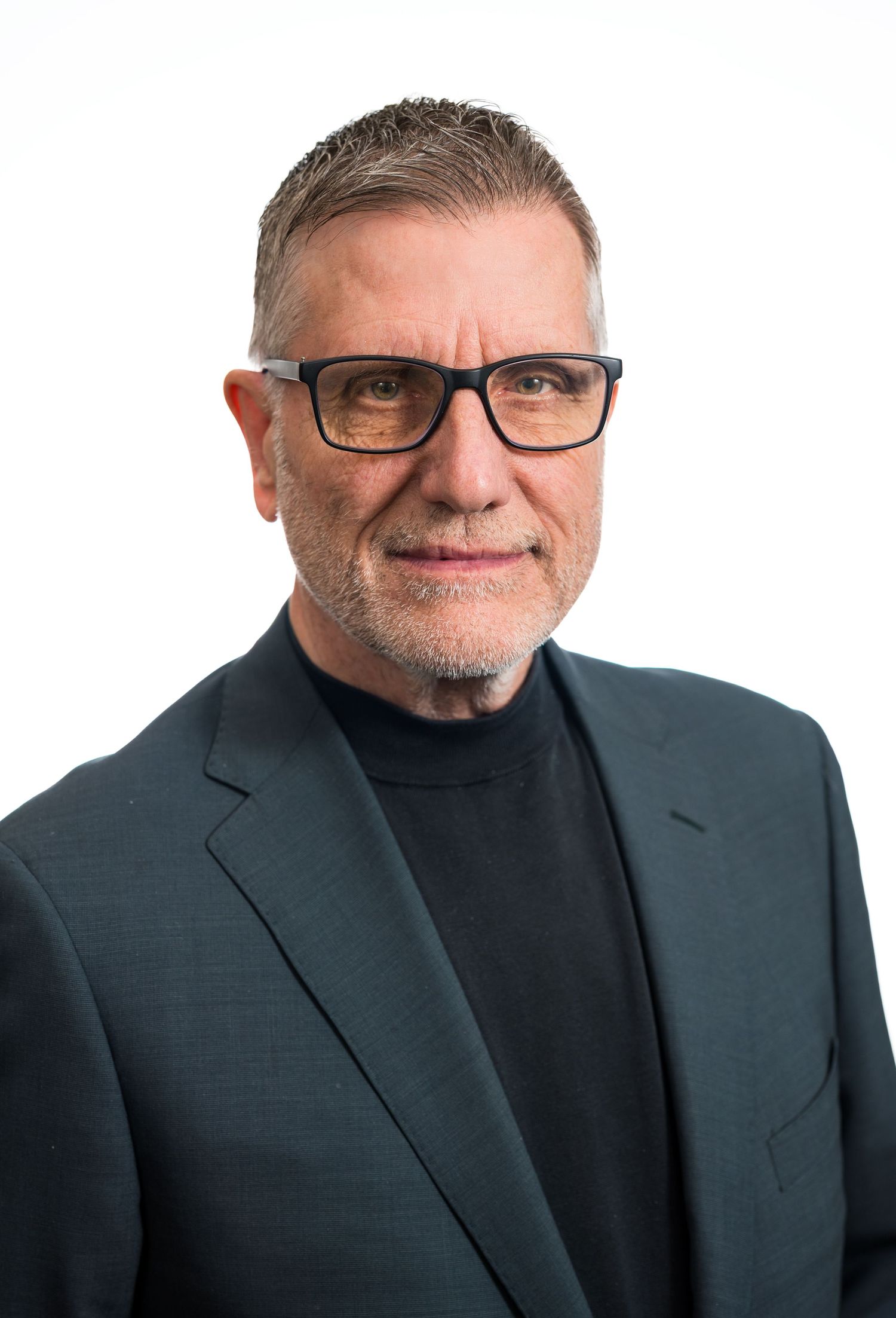Professional headshot of a middle-aged man with glasses, gray hair, and a beard wearing a dark blazer.