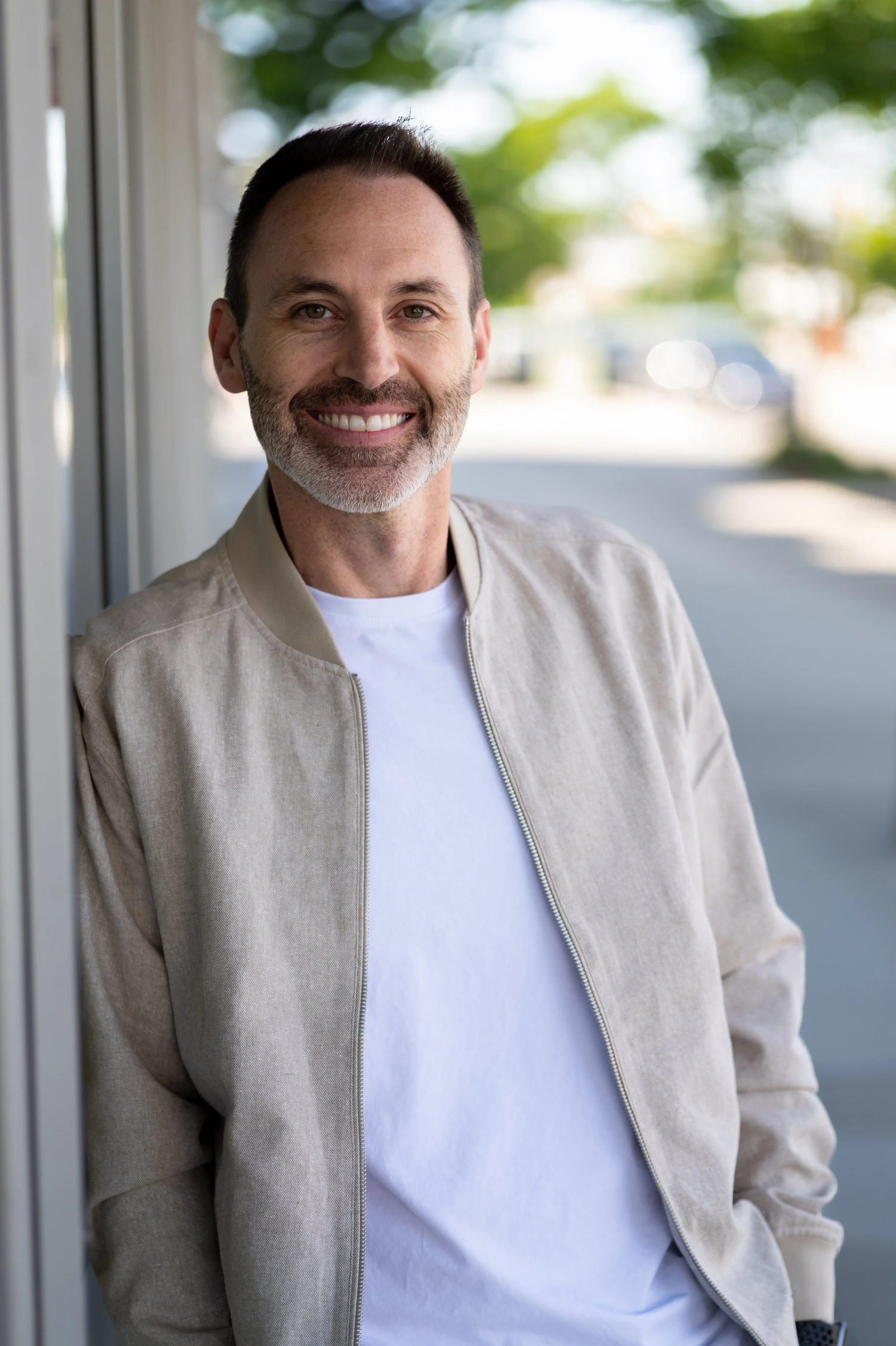 Person wearing a beige blazer and white t-shirt poses against a bright outdoor background in multiple shots.