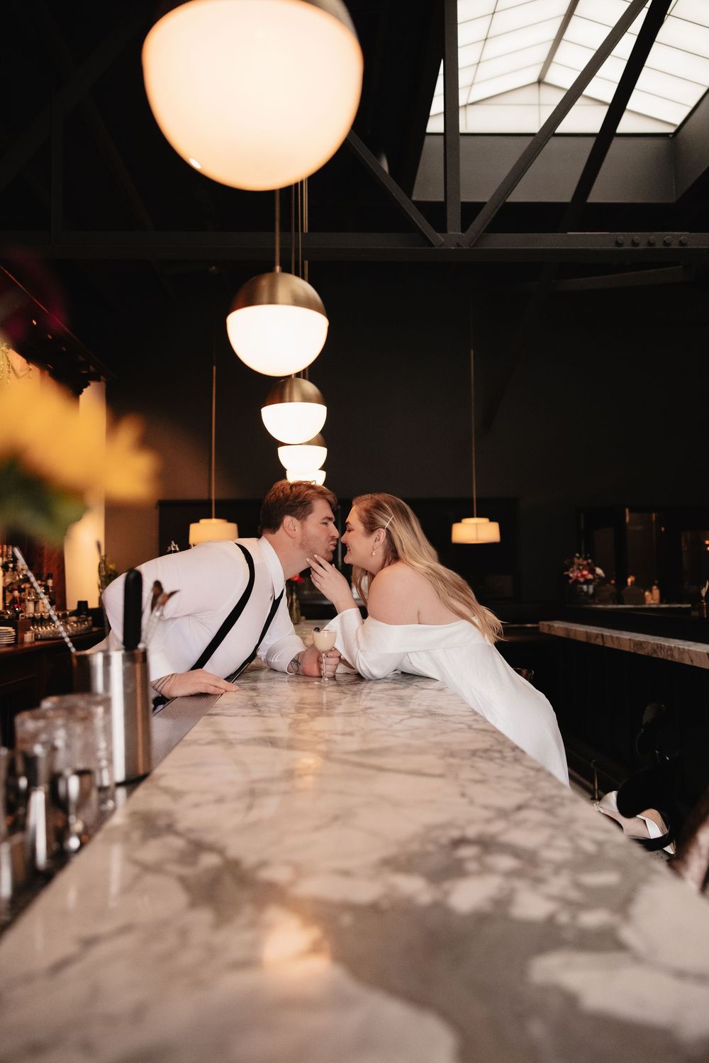 A couple shares an intimate moment at a marble bar counter under warm pendant lighting in an elegant venue.