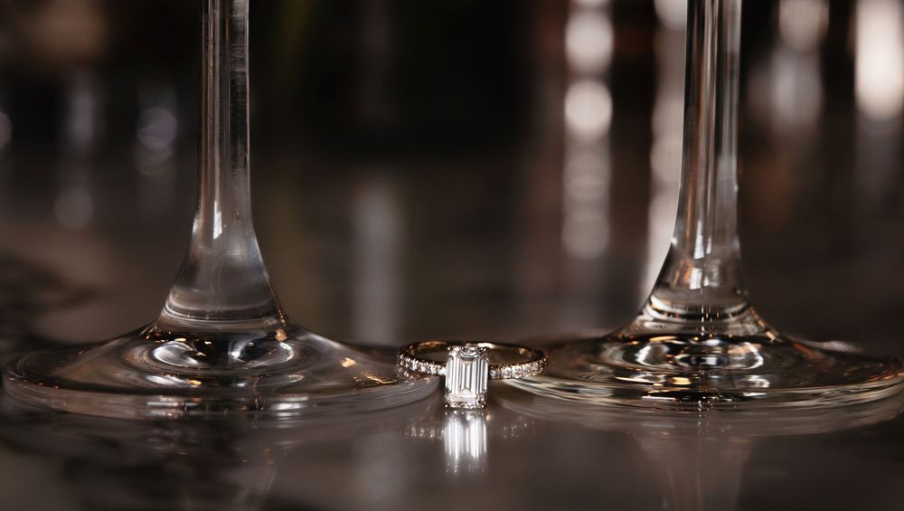 Wedding rings and jewelry displayed in an artistic macro shot on a reflective glass surface.