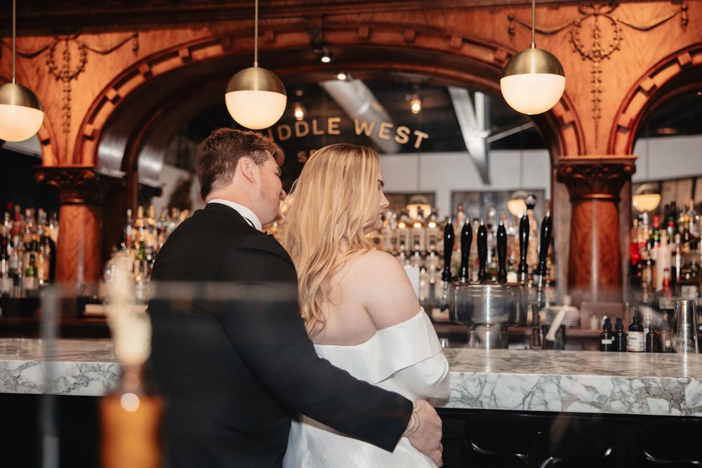 A romantic couple shares an intimate moment at an elegant bar with warm lighting and glassware in the background.