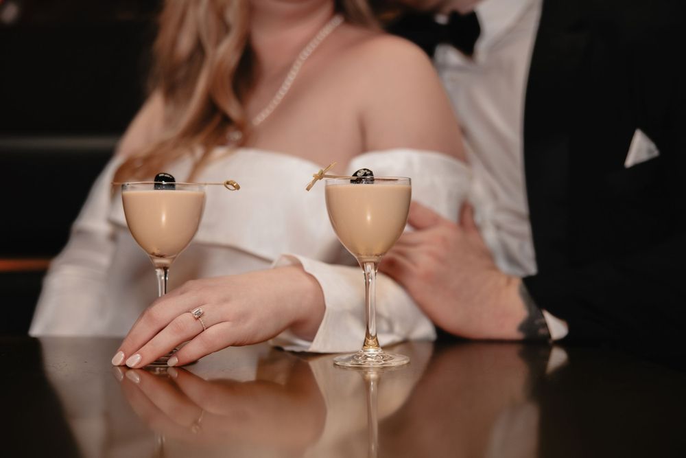 Two elegant cocktail glasses with creamy beige drinks sit on a reflective surface at a romantic evening setting.
