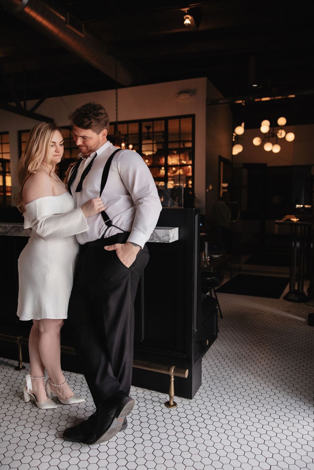 A romantic couple sharing an intimate dance moment on a black and white tiled floor in a dimly lit venue.