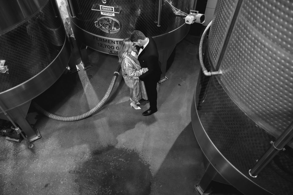 Vintage black and white photo of a worker inspecting large industrial brewing tanks in a brewery.