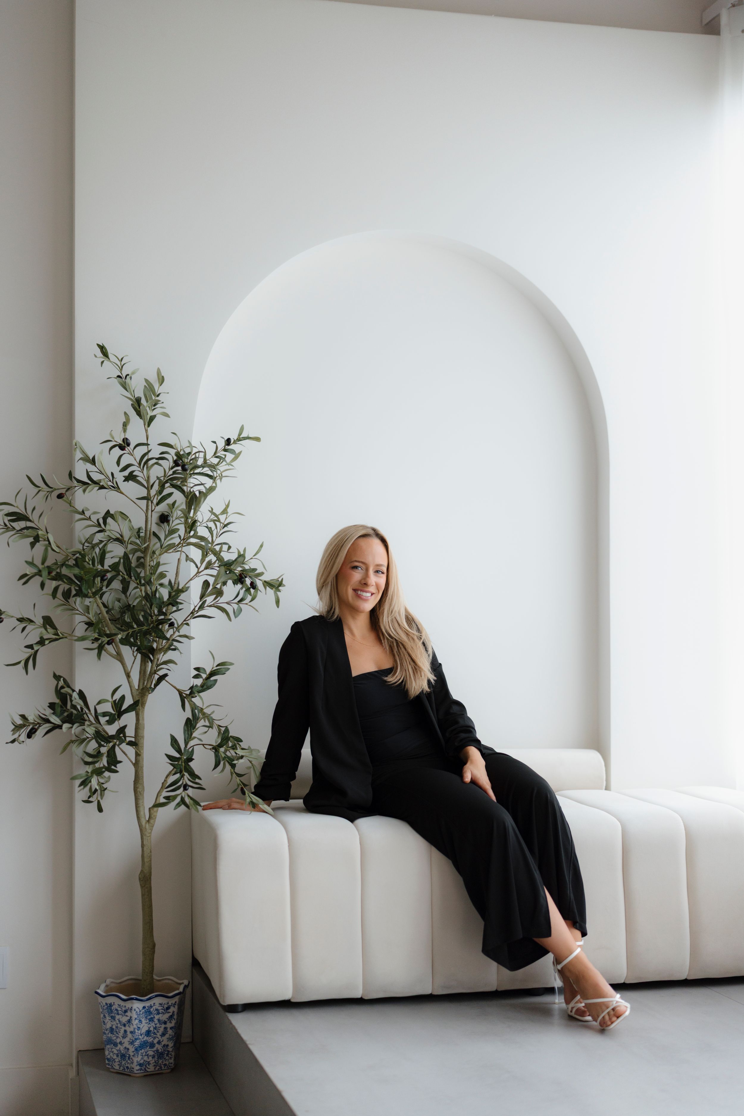 Minimalist white studio setting with curved walls, potted plants, and modern seating arrangement in monochromatic style.