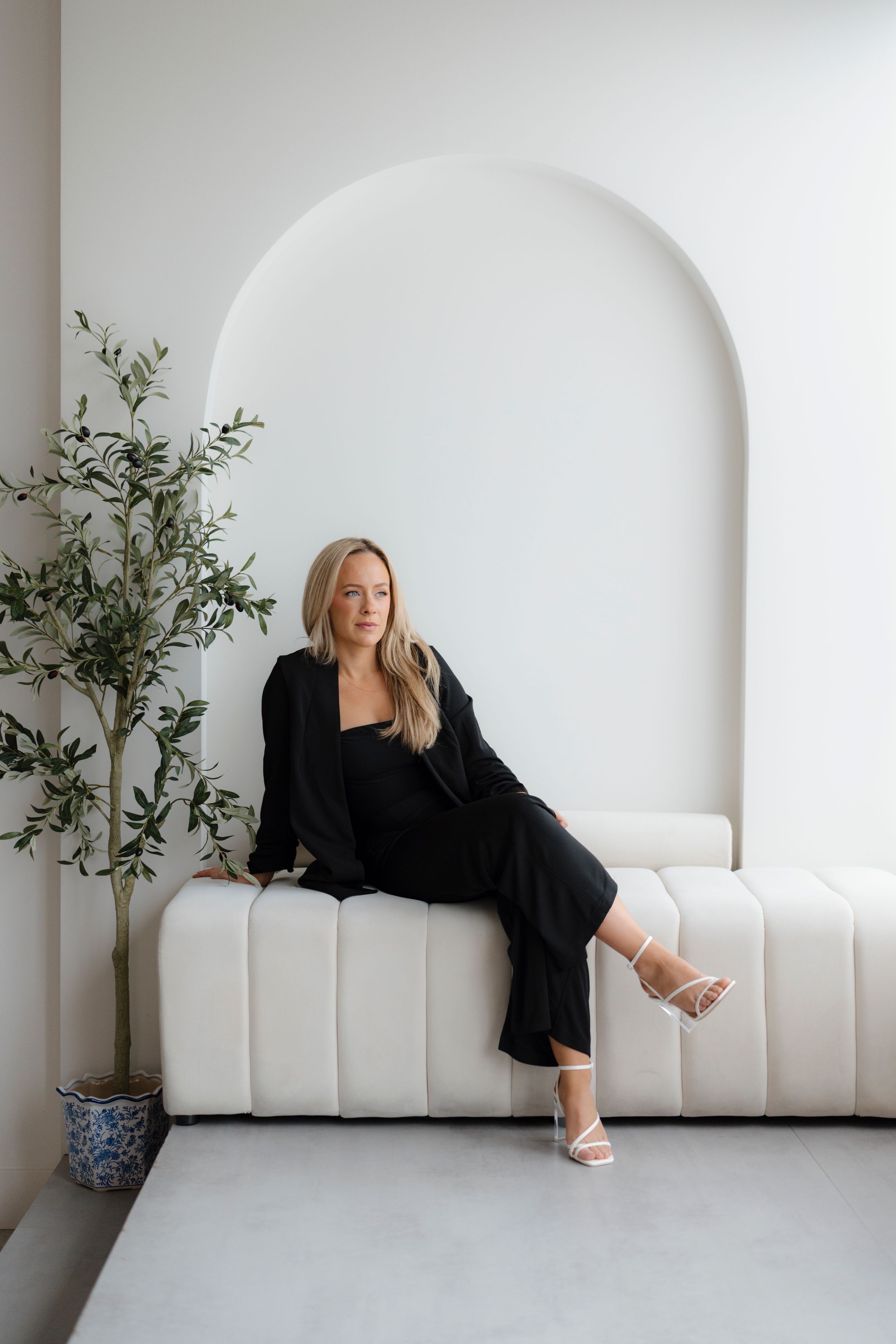 Woman in black ensemble lounging on modern white bench under arched wall.