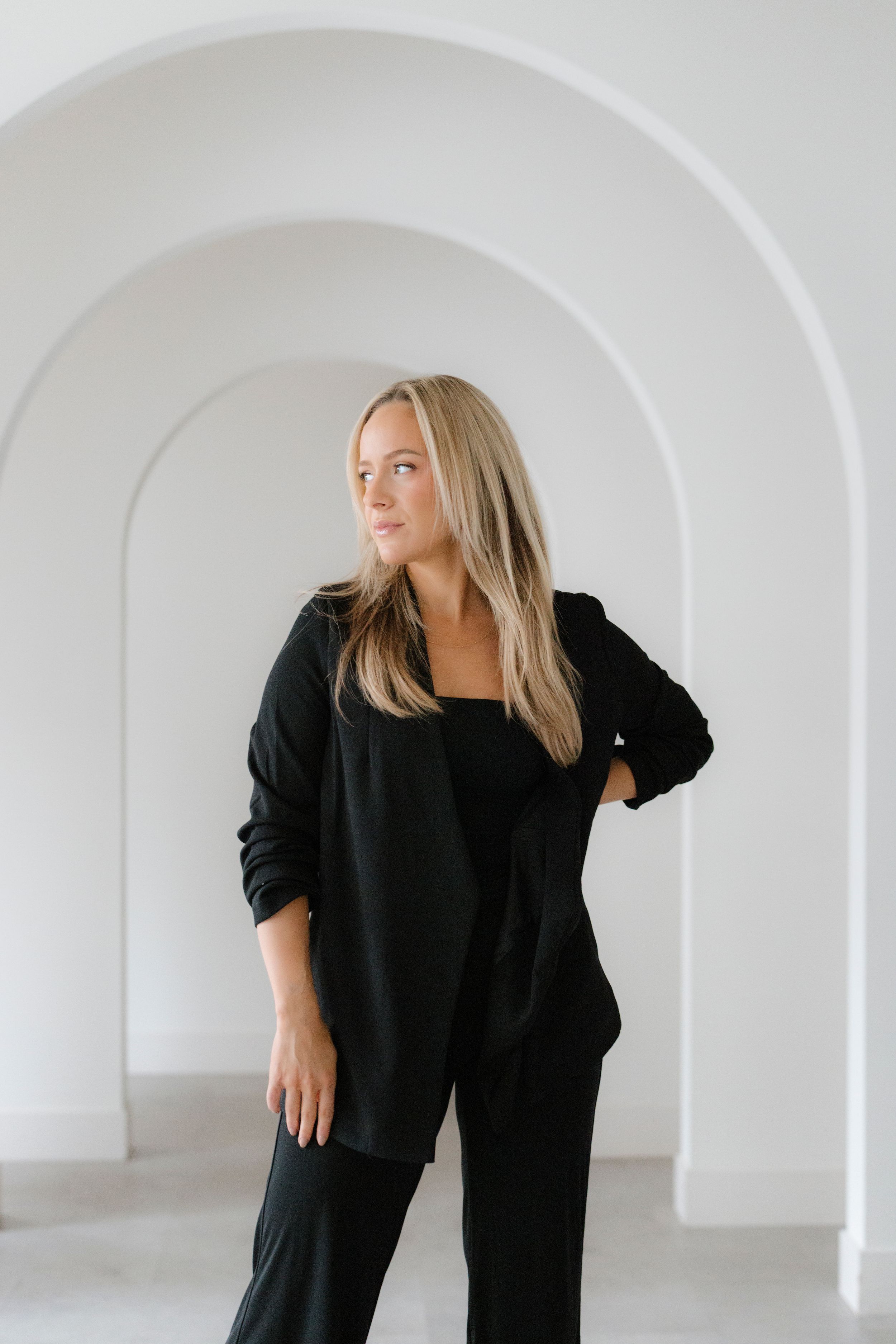 Fashion photoshoot featuring black outfit ensemble in minimalist white architectural space.