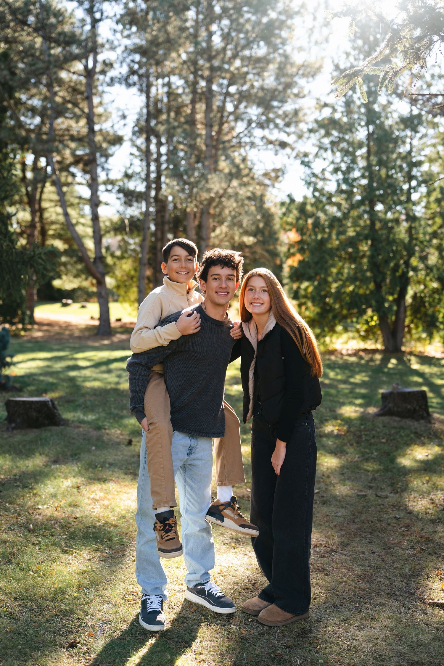 Young person in blue patterned button-down shirt and dark pants poses confidently outdoors in warm sunlight.