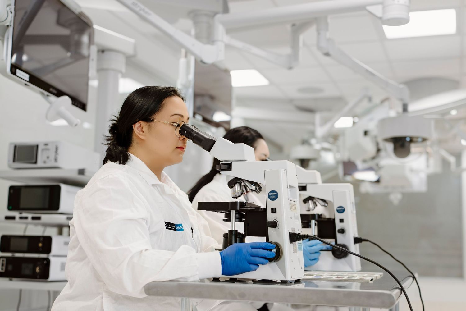 Scientists in white protective suits work with microscopes in a modern laboratory setting.