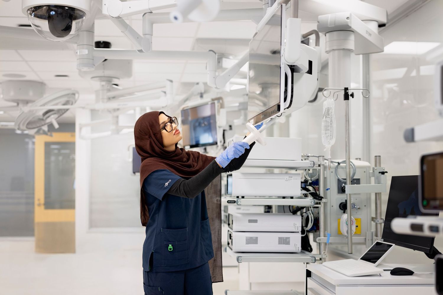 Dental professional adjusting overhead equipment in a well-lit clinical setting with modern dental chairs.