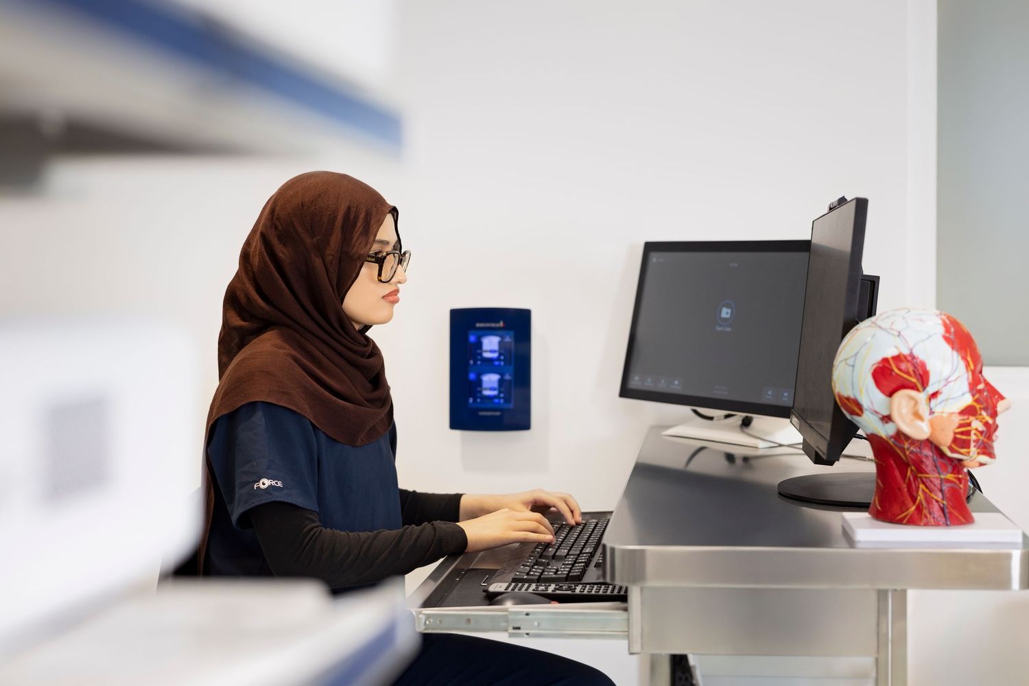 A person wearing a headscarf works at a computer desk in an office setting.
