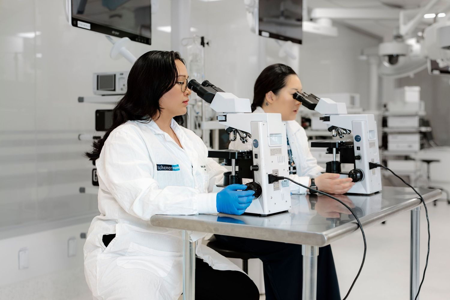 Scientists in white lab coats work with microscopes in a modern laboratory setting.