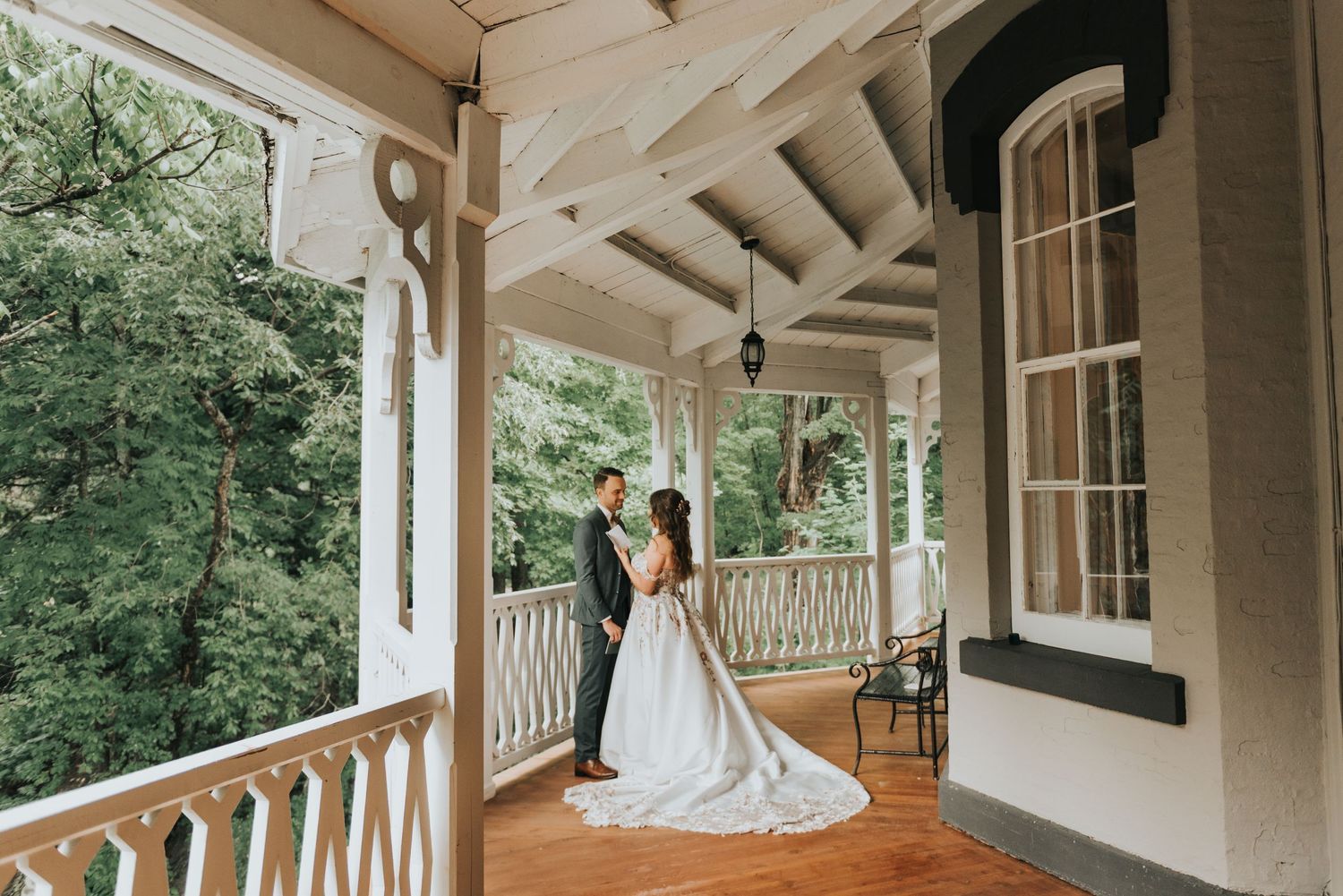 A couple shares an intimate moment on a rustic covered porch with white railings and wooden beams.