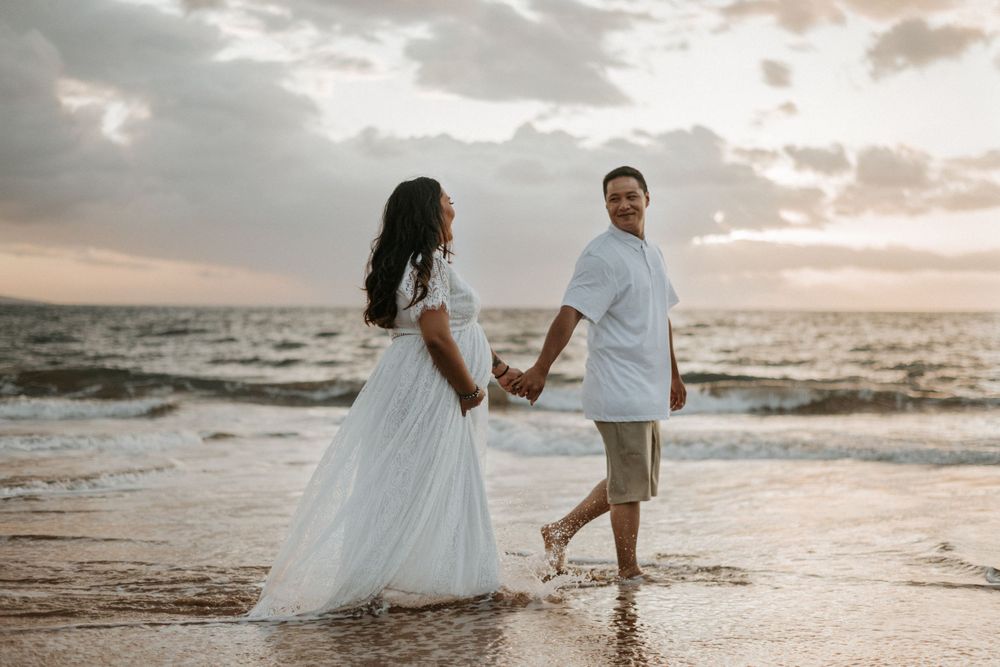 Couple walking through ocean waves during golden hour beach photo session.